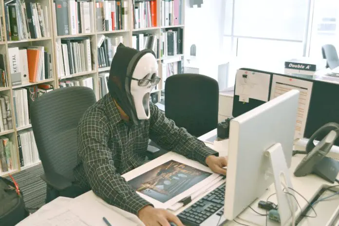 person wearing scream mask and black dress shirt while facing computer table during daytime