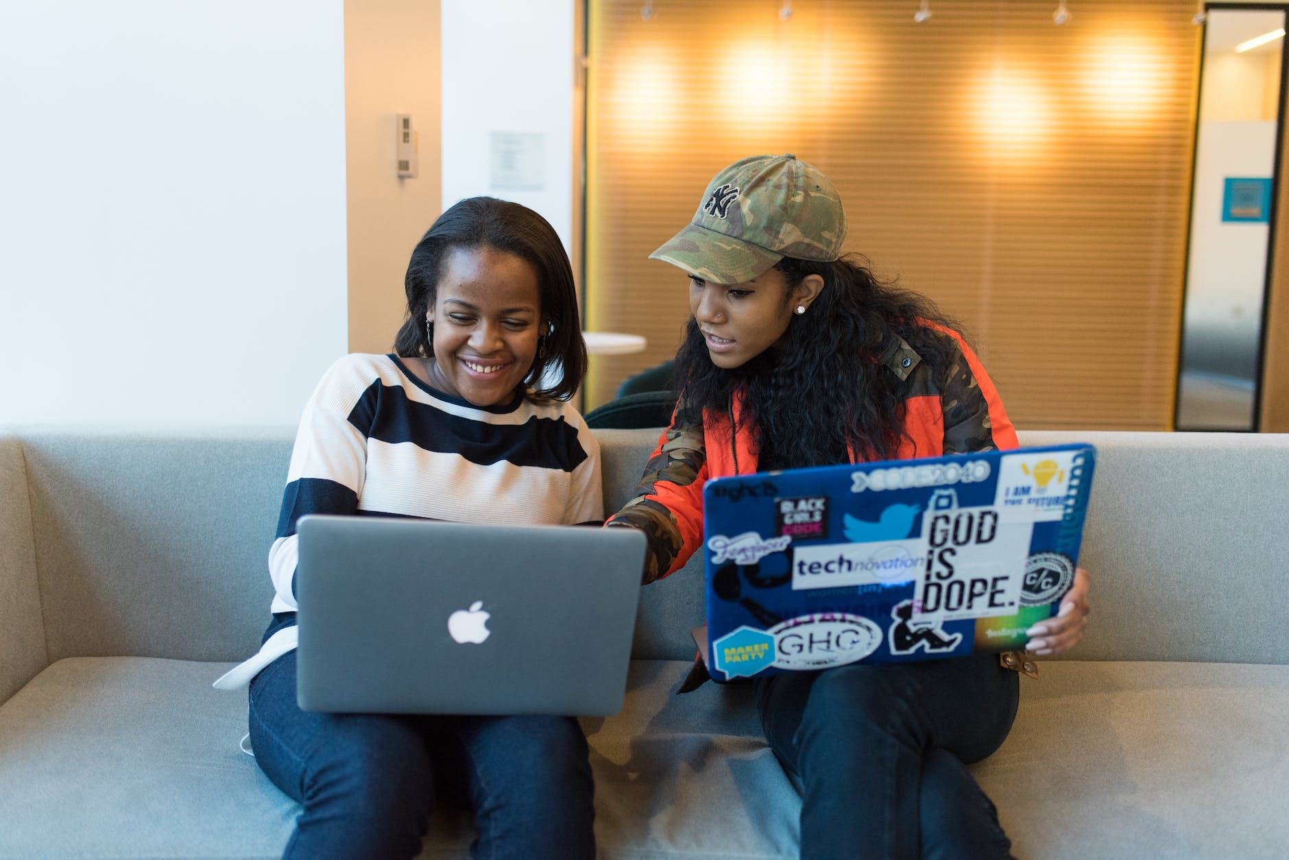 two woman sitting on sofa while using laptops