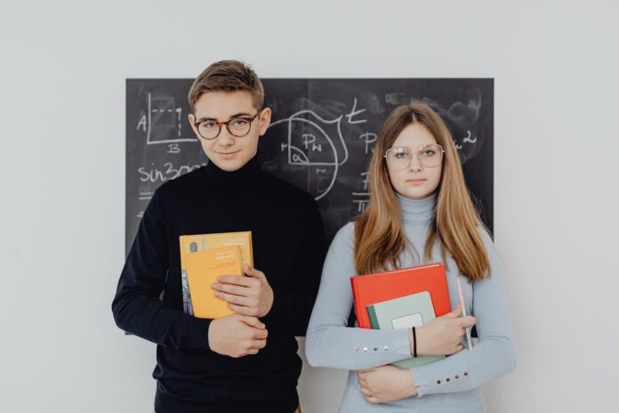 two teenagers with books against a blackboard