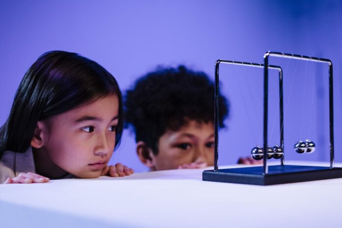boy and girl looking at newton s cradle and hiding behind the table