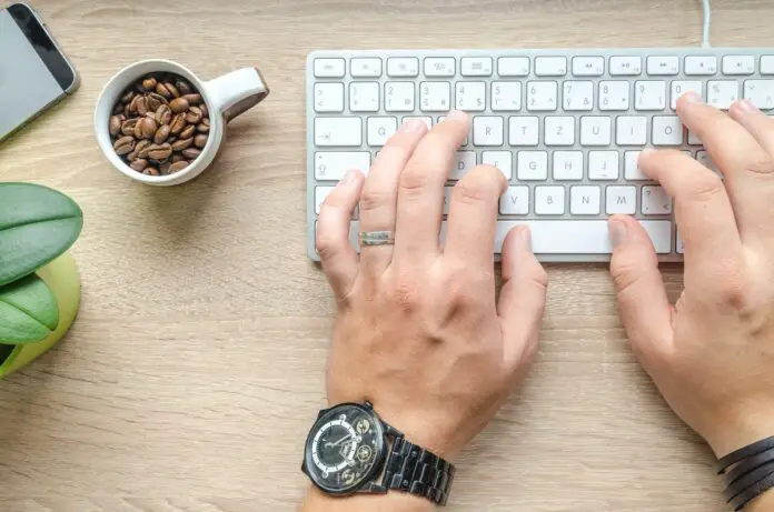 person using silver apple magic keyboard beside of white ceramic mug with coffee beans