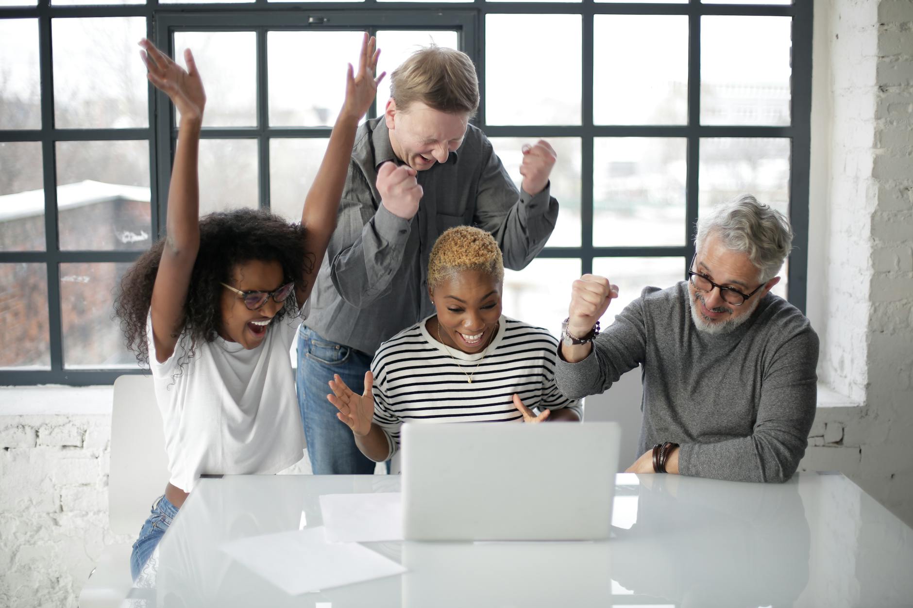 excited multiracial colleagues enjoying triumph together in front of laptop in office