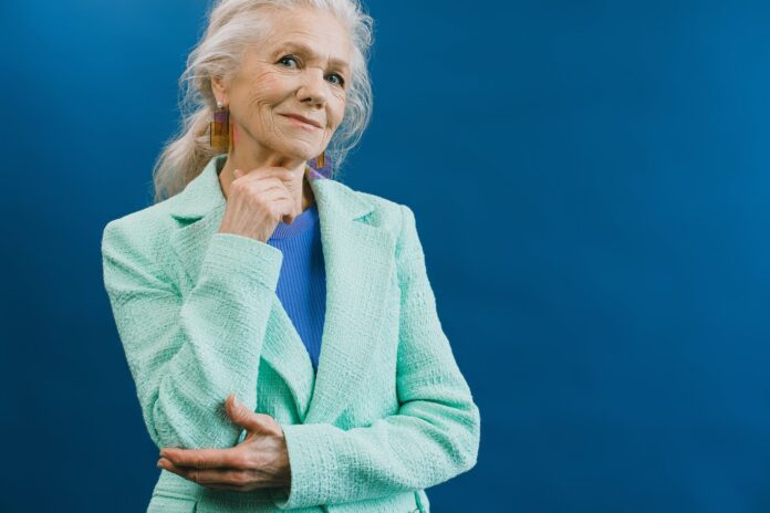 senior woman in green jacket standing against blue background